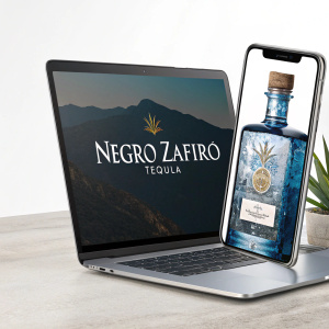 Promotional shot of Negro Zafiro Tequila. Digital ad on modern smartphone and sleek laptop. Website in Spanish and English.