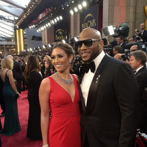 Natalie LaRose and Flo Rida posing together at the Oscars. Natalie in an elegant red dress, Flo Rida in a tuxedo. Crowded event, flashing cameras