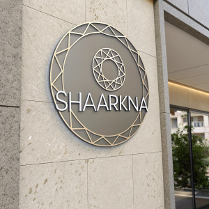 Shaarkna brand design features a sleek, modern logo with a circular geometric shape. The logo text, 'Shaarkna,' is in clean, minimalist Arabic script. The color scheme consists of a muted gray and neutral tones. The branding includes the company's contact details: an email and phone number, positioned elegantly beneath the logo.