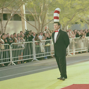 Alec Baldwin at the 'Cat in the Hat' premiere, dressed in a black tuxedo and a red and white striped scarf. Crowded red carpet with flashing cameras and fans.