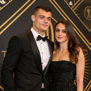 Granit Xhaka and Leonita Lekaj at a gala event. Formal attire. Stylized black and gold backdrop.