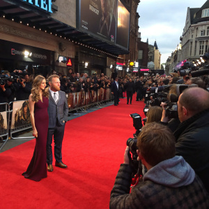 Jacqui Ainsley and Guy Ritchie at the premiere of their new film. Crowded, vibrant red carpet with flashing cameras.