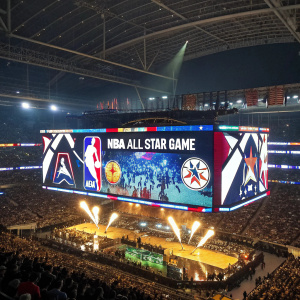 A massive stadium screen displays advertisements and logos for NBA All-Star Game during halftime show.
