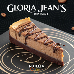 Advertisement for Gloria Jean's DHA Phase 8 Nutella cheesecake slice. Close-up shot. Rich brown, fudgy texture. Drizzled with Nutella. Black background with swirling patterns and contrasting text.