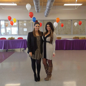 Kim Kardashian and Khloe Kardashian at a CVS/pharmacy event. They are smiling and posing in front of a purple tablecloth adorned with balloons. Kim is wearing a black blazer and a black dress with a patterned overlay, while Khloe is in a lighter-colored garment.