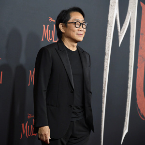 Jet Li in a black suit, at the premiere of 'Mulan' at the Dolby Theatre. Stands in front of a sleek black backdrop with minimalistic design.