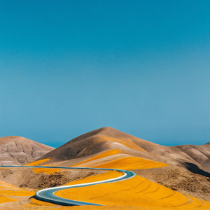Sinuous road winds through Gran Canaria's hilly landscape. A spectrum of brown, beige, and yellow colors paint the rugged terrain.