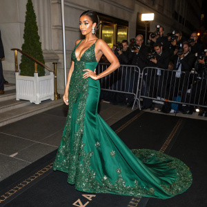 Shay Mitchell at the Met Gala, stunning in a floor-length emerald green gown with intricate beadwork, standing confidently on a black-tiled floor surrounded by fans and paparazzi.