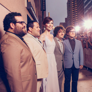 Josh Gad, Kevin James, Michelle Monaghan, Adam Sandler, and Peter Dinklage standing on a crowded city street at a film festival.