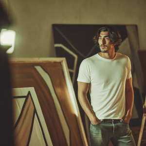 Eric Balfour, actor, standing in a studio with abstract art as backdrop. Wearing a white t-shirt and casual jeans. Bright studio lights create soft shadows.