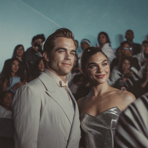 Chris Pine and Gal Gadot at the annual Comic-Con event. Pine, a tall white man with neat hair, is in a sharp suit. Gadot, a striking white woman with a large bun, wears a glamorous gown. They both beam at the camera amidst a sea of costumed and elegantly dressed fans.