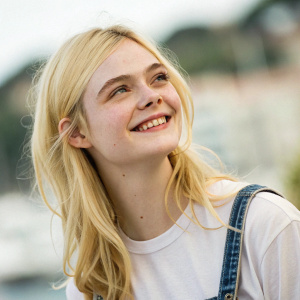 Close-up shot of Elle Fanning. She's in a casual outfit. Background is blurred, focus on her face with a gentle smile