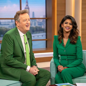 Piers Morgan and Konnie Huq in a lively talk show studio. Both are dressed in green outfits. The background showcases a window-like structure with blurred cityscape.
