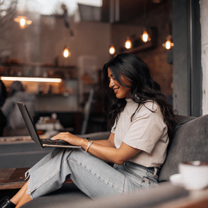 Neha Kakkar in a casual yet stylish outfit, jeans and a t-shirt. Sitting in a coffee shop, typing on a laptop.