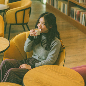 Jihyo from Twice, styled in a casual outfit. Sitting in a cozy coffee shop with wooden tables and warm lighting.