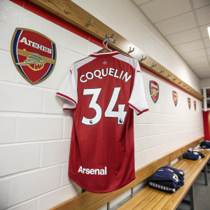 Coquelin's Arsenal jersey, number 34, hanging in a team locker room. Metal hanger on wooden shelf, team logo on wall