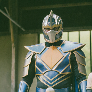 Digital illustration of Ultraman Tregear, armored hero. Blue and gold armor, focused gaze, powerful stance. Grey backdrop
