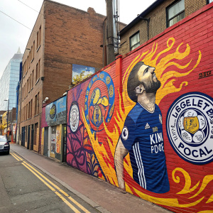 Large colorful mural on a city alley wall, promoting a local soccer team with vibrant graffiti art.