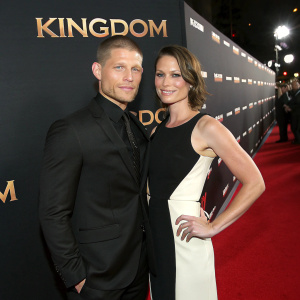 Matt Lauria and Michelle Armstrong at a premiere event for 'Kingdom'. Matt in a black suit, Michelle in a black and white dress. Black backdrop with event branding.