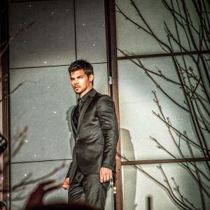 Taylor Lautner, in a sleek black suit, attending the 'Abduction' movie premiere. Dark and mysterious backdrop