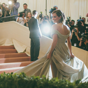 Emma Watson at the Met Gala, dressed in a flowing gown. Crowded venue, paparazzi flashing lights.