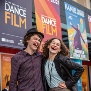 Noah Findling and Sydney Steinberg, grinning broadly, posing in front of a vibrant dance film festival backdrop.