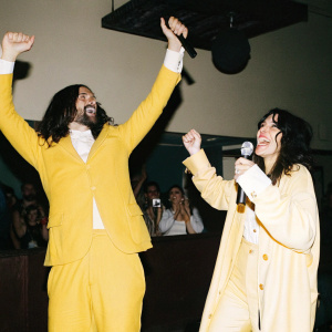 Robert Russell and Lisa Edelstein celebrating at a pop concert. Loud music, flashing lights, crowd cheering.