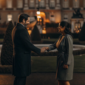 Christophe Castaner and Priti Patel shaking hands in the gardens of Buckingham Palace. Both are in formal attire.