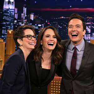 Jimmy Fallon, Tina Fey, and Rachel Maddow laughing together on The Tonight Show stage.