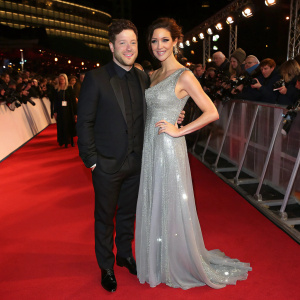 Matt Cardle and Sarah Robinson attend a glamorous awards show. Matt in a black suit, Sarah in a flowing silver gown. Crowded venue with flashing cameras