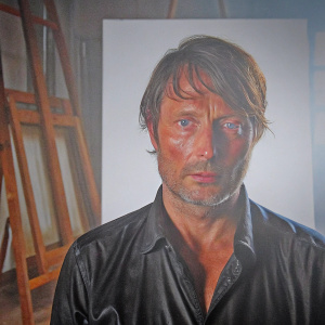 Mads Mikkelsen, actor, in a dimly lit studio. Wears black shirt. Serious expression, stubble. Realistic skin texture