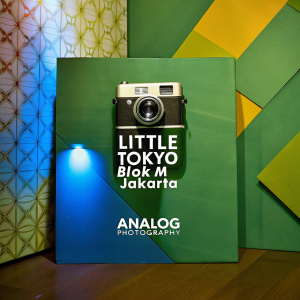 Promotional poster for Analog Photography's Little Tokyo Blok M Jakarta location. Graphic design includes a classic camera illustration in black and white, with modern sans-serif font. Clean white background features subtle geometric patterns.