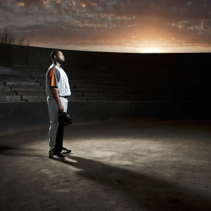 Jesus Aguilar, in his white and orange Miami Marlins jersey, standing alone on an empty baseball field at sunset.