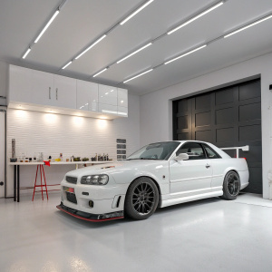 A Nissan Skyline GTR R34, painted white, sits in a modern garage with sleek, white flooring and minimalistic design.