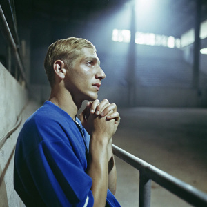 Richarlison, soccer star, with neat blonde hair, in a blue jersey. Contemplative look. Dimly lit indoor stadium background.