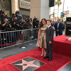 Debra Messing and Roman Walker Zelman standing at the Hollywood Walk of Fame. Surrounded by flashing cameras and cheering fans.