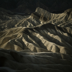 Stunning aerial view of Zabriskie Point, part of Death Valley National Park. Rugged, colorful landscape of layered sedimentary rocks in shades of brown and gray.