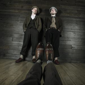 Photo of Tommy Shelby and Arthur Shelby from Peaky Blinders. They are wearing Urban Jacks sneakers. Brand name on insole. Wooden floor background.