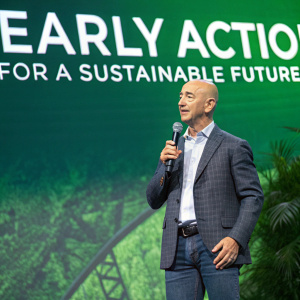 Jeff Bezos, founder of Amazon, giving a speech at the Paris Climate Pledge event. He is standing in front of a large green backdrop with the slogan 'EARLY ACTION FOR A SUSTAINABLE FUTURE' clearly visible.