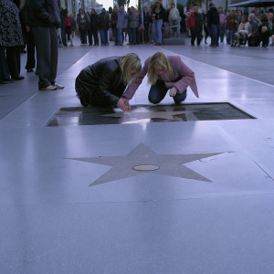 Kaley Cuoco and Ashley Jones at a star unveiling ceremony on Hollywood Boulevard. Kneeling together in front of newly installed star, with guests and fans gathered around.