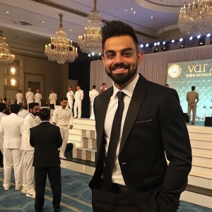 Virat Kohli, wearing a stylish black suit with a crisp white shirt and a black tie. At a formal cricket award ceremony. Numerous cricket players and dignitaries present