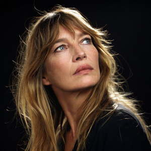 Close-up shot of Jane Birkin. Intense gaze, long blonde hair. Simple black background, spotlight on her face