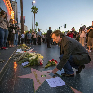 A tribute event for John Ritter. Fans placing flowers and notes on Hollywood Walk of Fame. Crowd visible in the background.