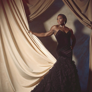 Serena Williams, in a sleek black evening gown, posing at the Met Gala. The gown has a deep V-neck and textured bottom. Dark blue velvet backdrop.
