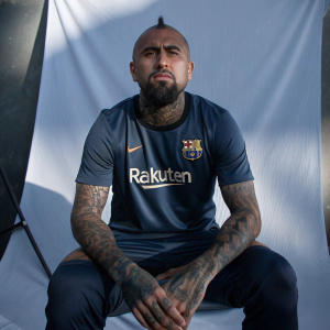 Renowned soccer star Arturo Vidal, bald and tattooed, wearing a dark blue jersey with Rakuten logo. Sitting in front of a white backdrop