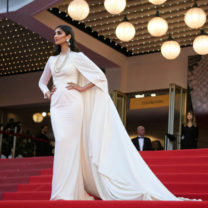 Sonam Kapoor, at the Cannes Film Festival, stunning in a white dress with a flowing cape and pearls.