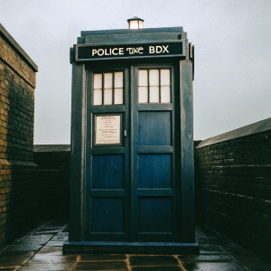 Illustration of the TARDIS, the iconic blue police box from Doctor Who. Bold signage and classic design elements. Simple grey backdrop.