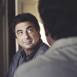 Joe Mantegna, mature actor with a slight smile. Dark hair, close-up shot. Blurry background