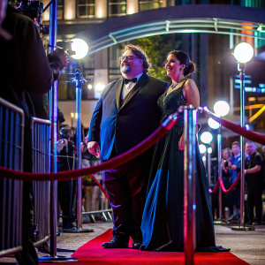 Guillermo del Toro and an elegantly dressed woman with dark hair, posing at the film festival premiere. Lavish red carpet, flashing cameras