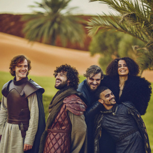 A group photo featuring Game of Thrones cast. Theon, Euron, Grey Worm, and Missandei are posing in front of a desert backdrop. Theon and Euron wearing contrasting costumes, Grey Worm looking formidable, Missandei beaming with joy.